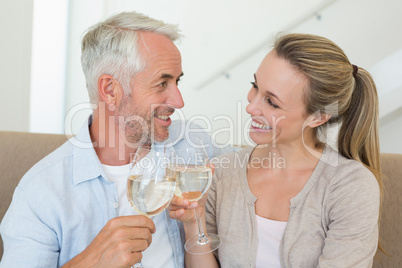 Happy couple sitting on couch toasting with white wine