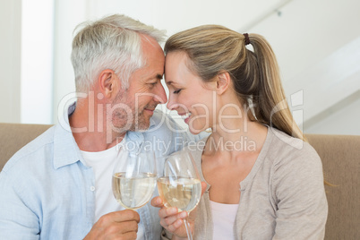 Happy couple sitting on couch toasting with white wine Happy couple sitting on couch toasting with white wine