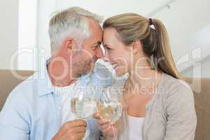 Happy couple sitting on couch toasting with white wine