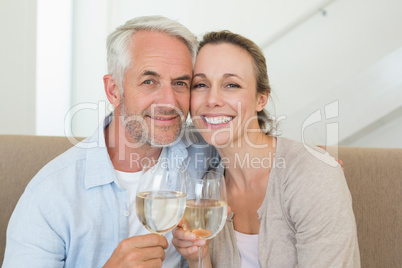 Happy couple sitting on couch toasting with white wine