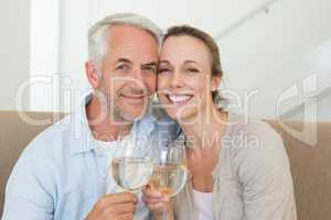 Happy couple sitting on couch toasting with white wine