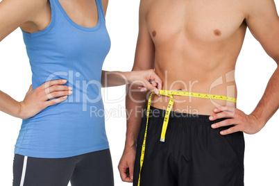 Mid section of a fit woman measuring mans waist