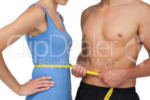 Mid section of a fit man measuring womans waist