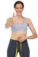 Fit woman measuring waist while gesturing thumbs up