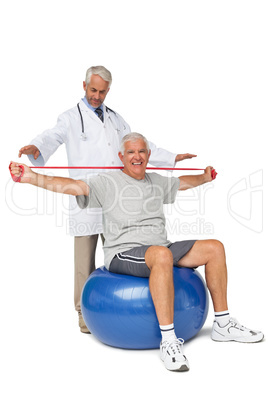 Mhysiotherapist looking at senior man sit on exercise ball with