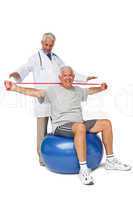 Mhysiotherapist looking at senior man sit on exercise ball with