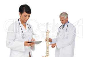 Doctor holding digital table with colleague by skeleton model