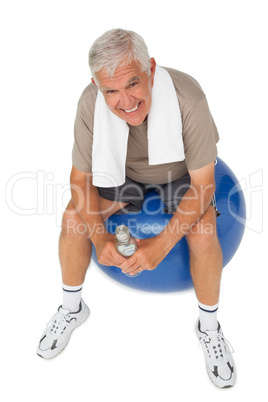 Happy senior man with water bottle sitting on fitness ball