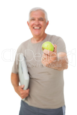 Cheerful senior man with an apple and scales