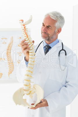 Mature male doctor holding skeleton model in his office