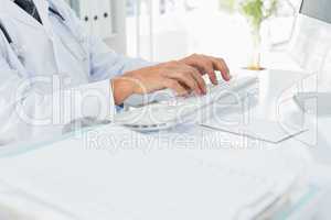 Mid section of doctor using computer keyboard at medical office