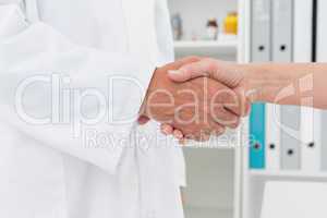 Mid section of a doctor shaking hands with patient