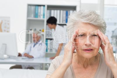 Senior patient suffering from headache with doctors at medical o