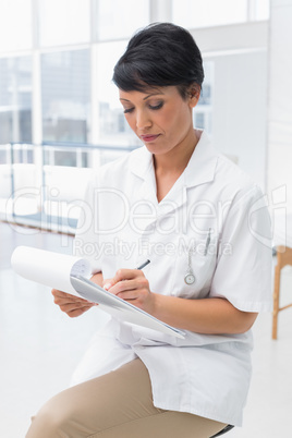 Concentrated female doctor writing on clipboard