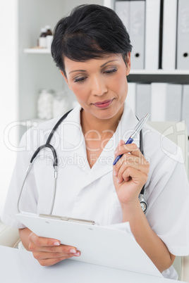 Concentrated female doctor writing on clipboard