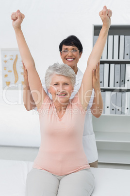 Female physiotherapist with senior woman raising hands