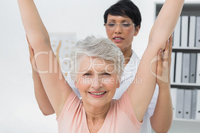 Female physiotherapist with senior woman raising hands