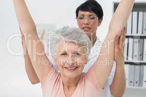 Female physiotherapist with senior woman raising hands