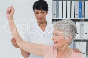 Physiotherapist assisting senior woman to stretch her hand