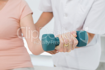 Mid section of physiotherapist assisting woman to lift dumbbell