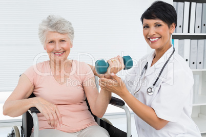 Physiotherapist assisting senior woman to lift dumbbell