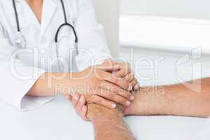 Close-up mid section of a doctor holding patients hands