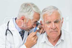 Male doctor examining senior patient's ear