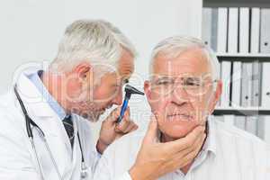 Close-up of a male doctor examining senior patient's ear