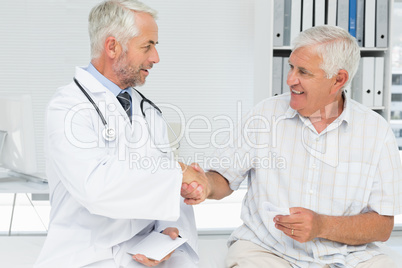 Smiling senior patient and doctor shaking hands