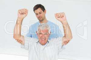 Physiotherapist assisting senior man to raise hands