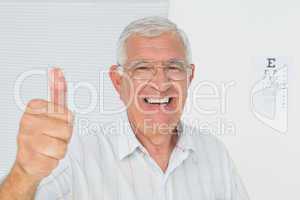 Smiling senior man gesturing thumbs up with eye chart in backgro