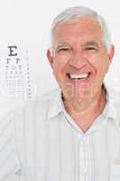 Portrait of smiling senior man with eye chart in background