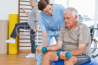 Female therapist assisting senior man with dumbbells
