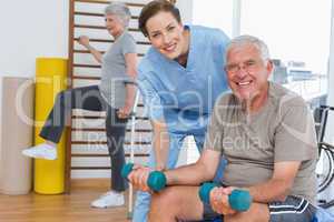 Female therapist assisting senior man with dumbbells