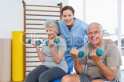 Female therapist assisting senior couple with dumbbells