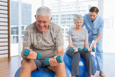 Female therapist assisting senior couple with dumbbells