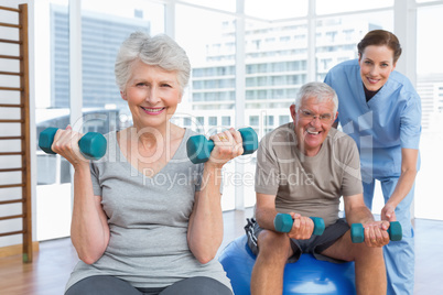 Female therapist assisting senior couple with dumbbells