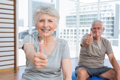 Senior couple gesturing thumbs up at medical gym