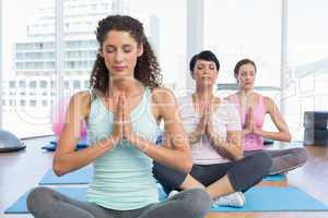 Women with eyes closed and joined hands at fitness studio