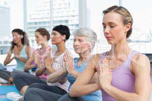 Class sitting with joined hands in a row at yoga class