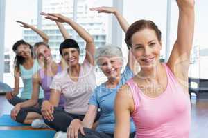 Trainer with women in row stretching hands at yoga class