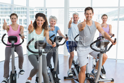 People working out at spinning class while gesturing thumbs up