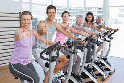 People working out at spinning class while gesturing thumbs up