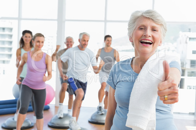 Senior woman gesturing thumbs up with people exercising