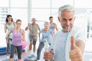 Senior man gesturing thumbs up with people exercising in fitness