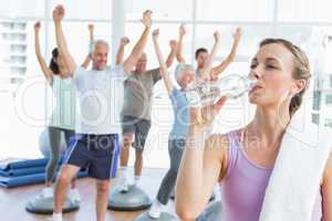 Woman drinking water with people stretching hands at fitness stu