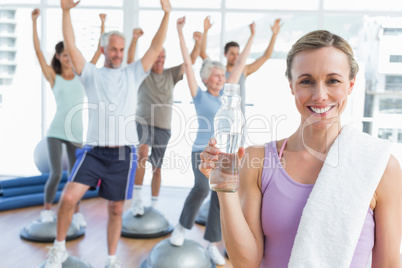 Woman holding bottle with people stretching hands at fitness stu