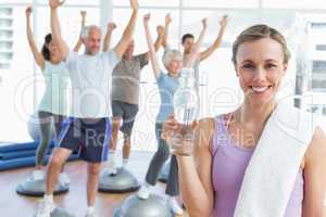 Woman holding bottle with people stretching hands at fitness stu