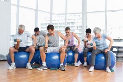 Fitness class with dumbbells sitting on exercise balls in gym