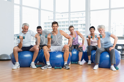 Fitness class with dumbbells sitting on exercise balls in gym